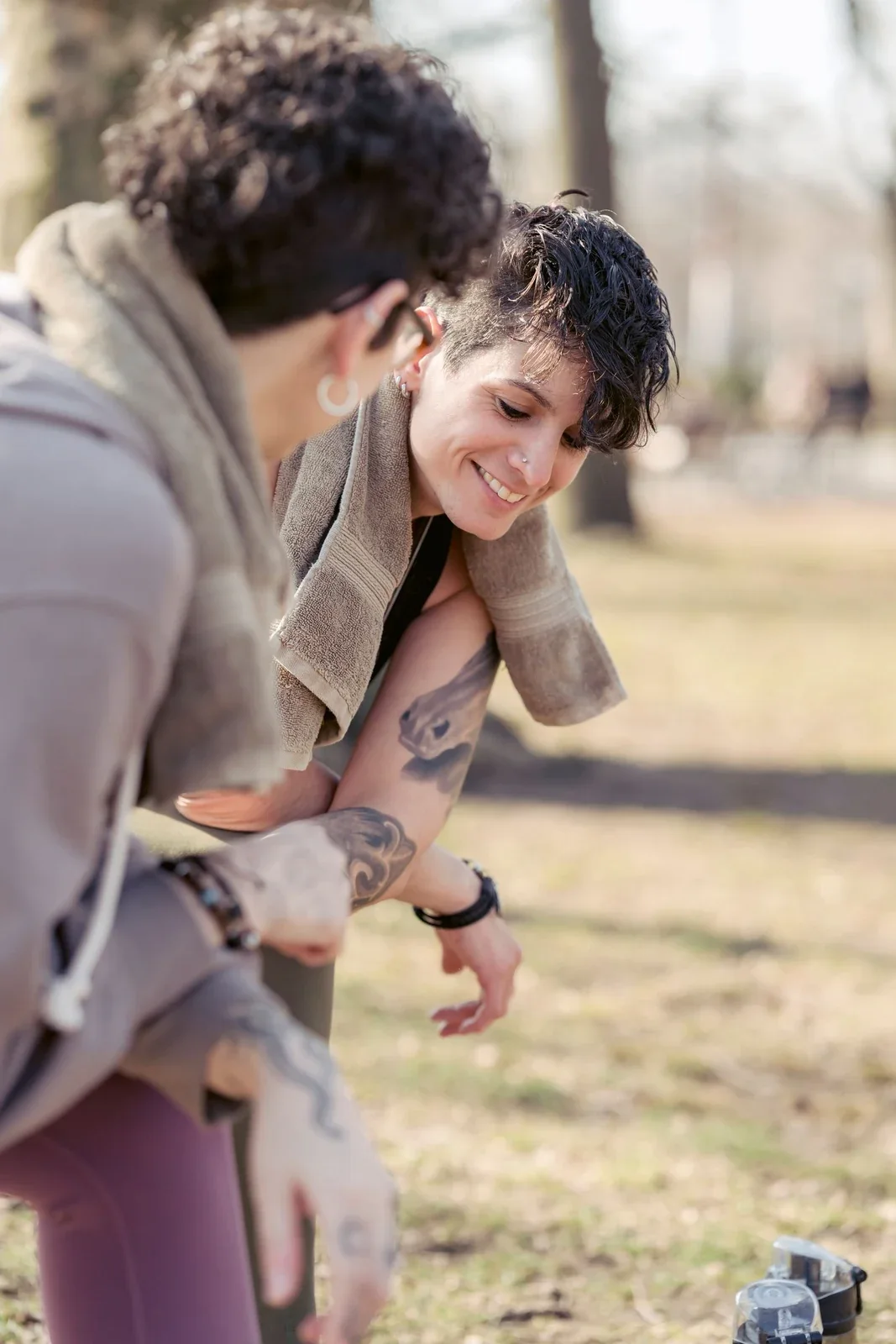 Two women resting and smiling together after exercising in a park.