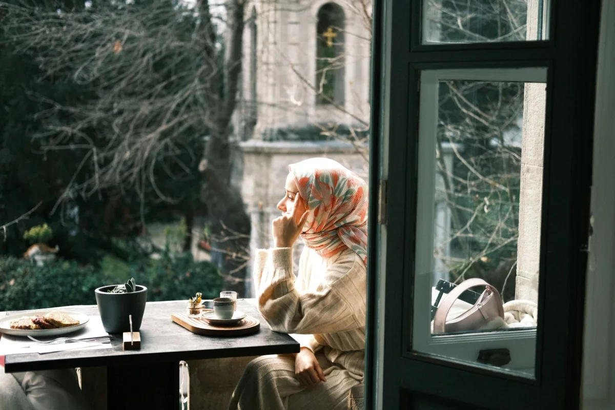 Woman in a patterned headscarf enjoying a quiet coffee by an open window.