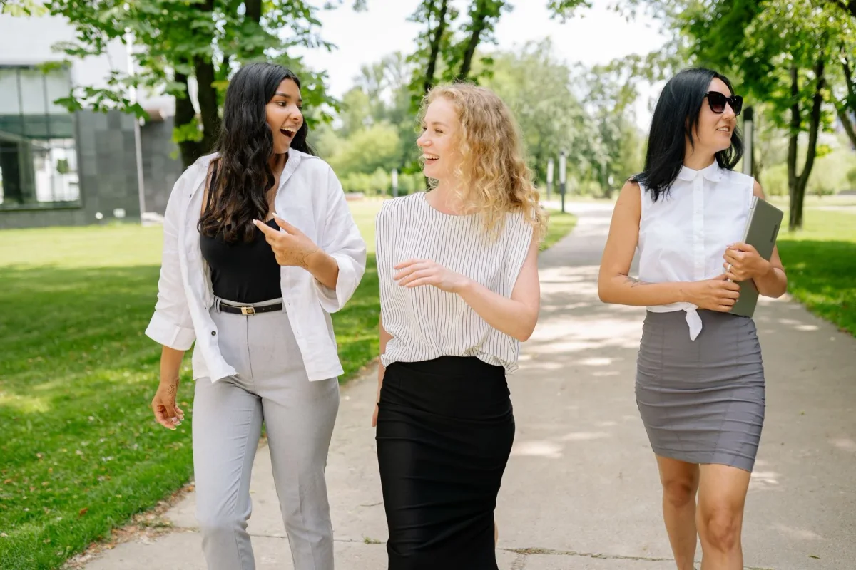 Three women talking while walking together on a park path.